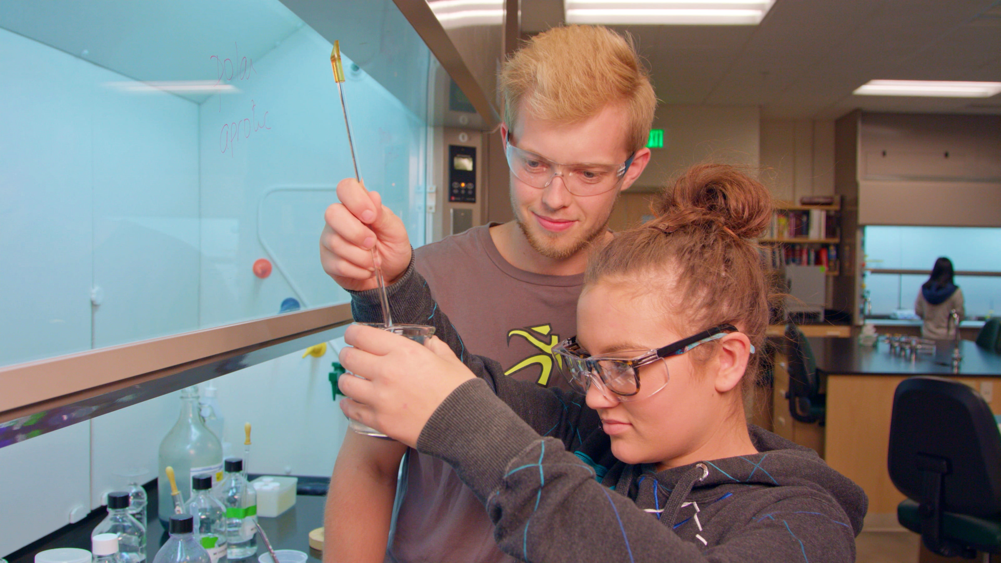  Two students wearing safety goggles work together in a science lab.