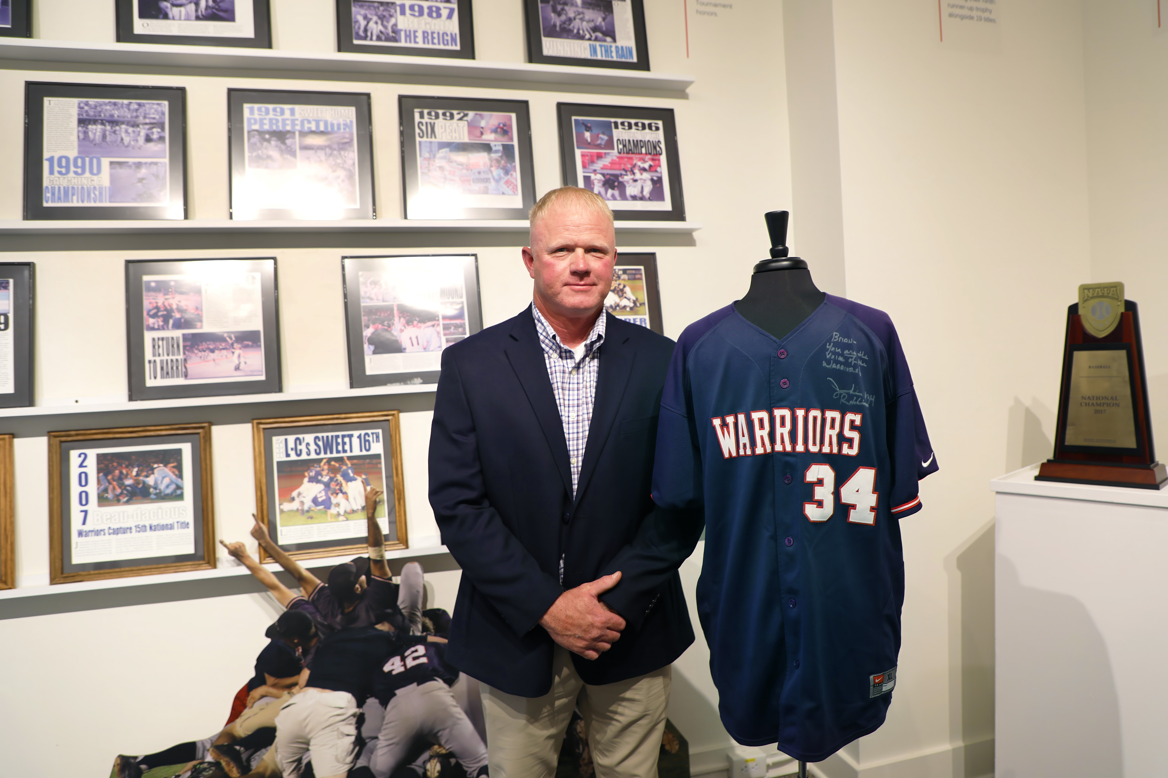 Jeremiah Robbins stands next to his Warrior baseball jersey that is on a mannequin 