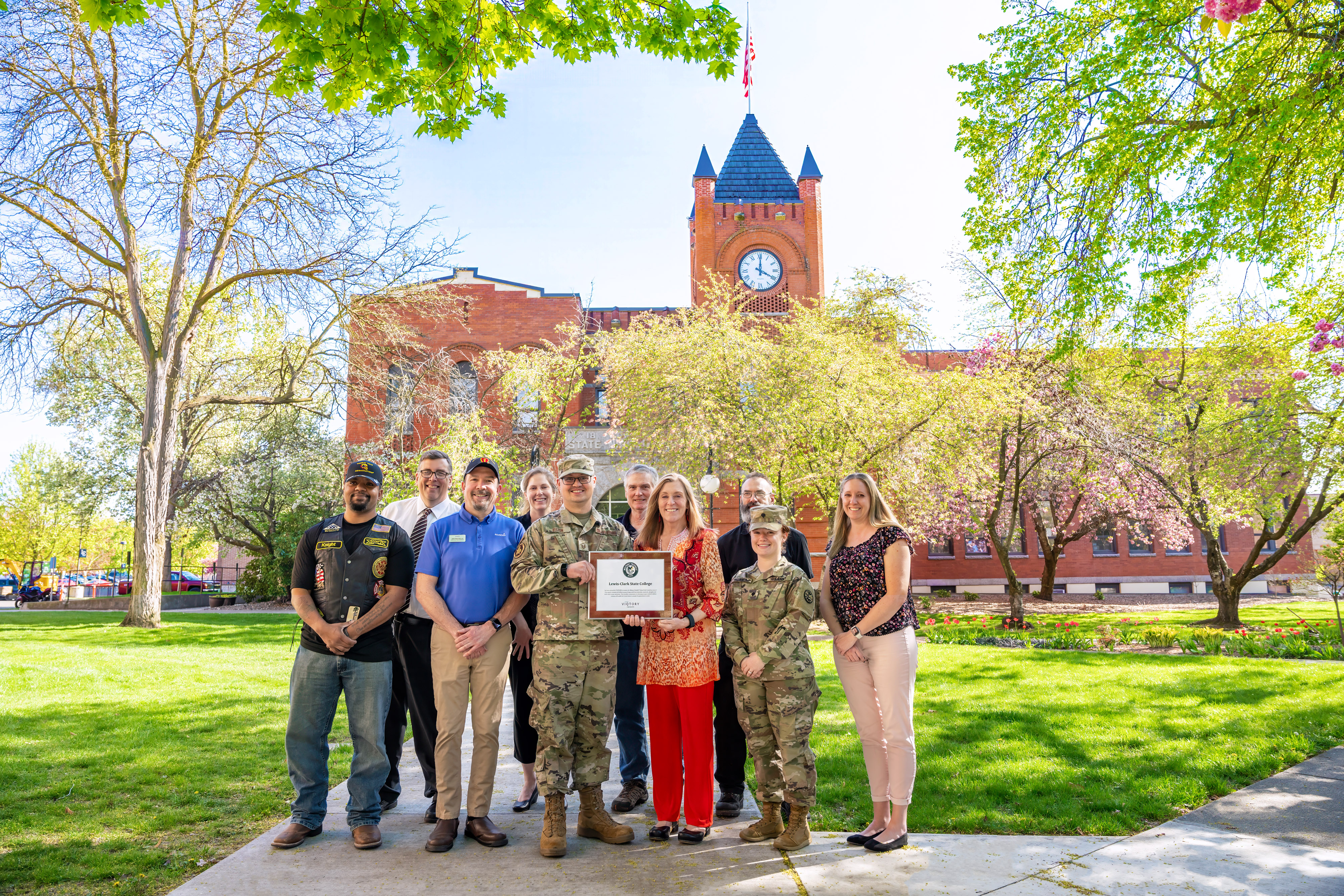 Group posed in front of LC State's Reid Centennial Hall Clock Tower with Military Friendly Gold Designation Plaque 