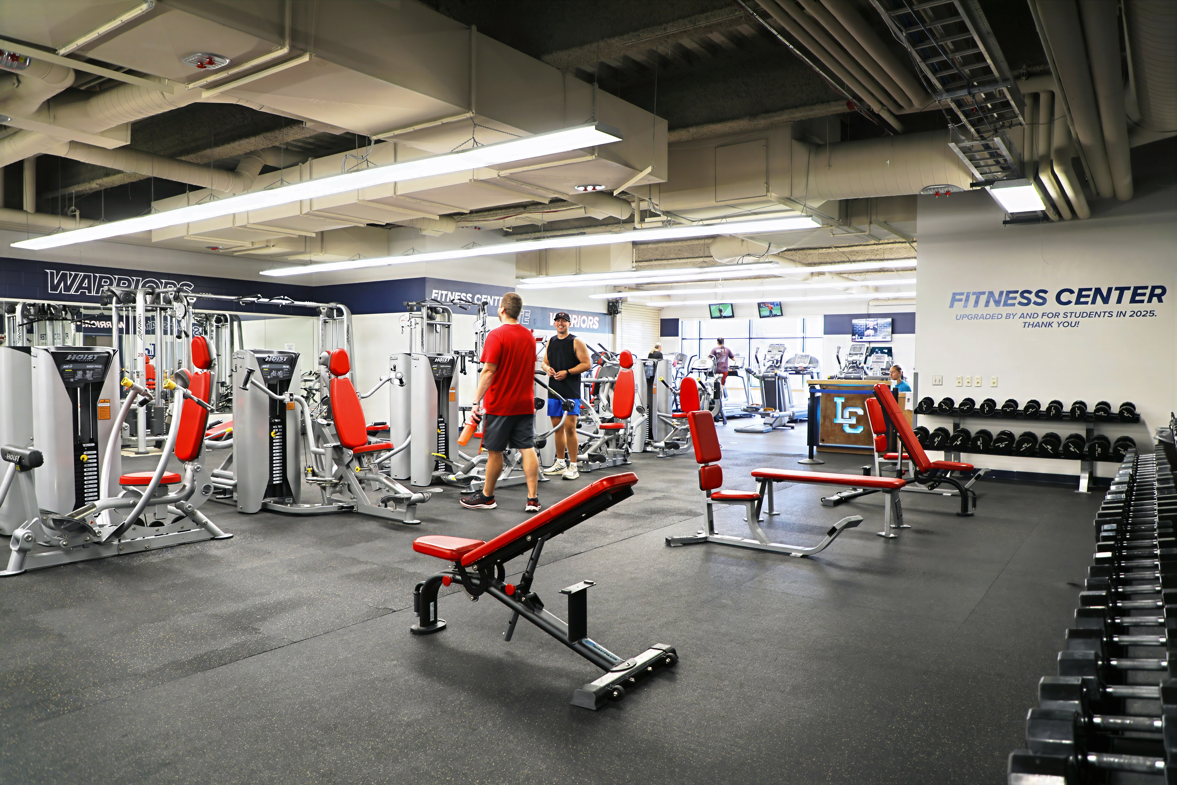 Inside of fitness center, two males talking by fitness equipment