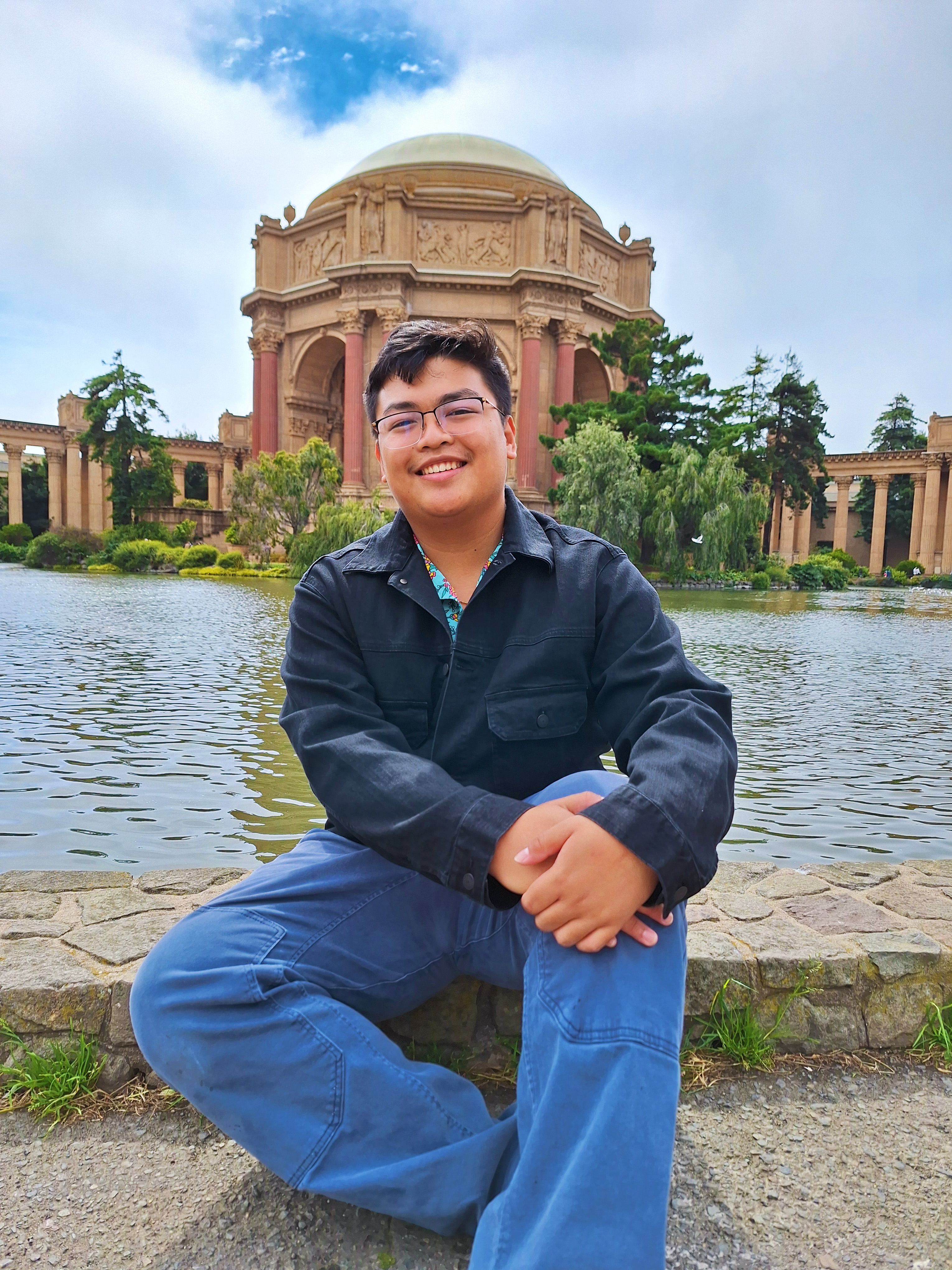 Student sitting in front of circular building and body of water