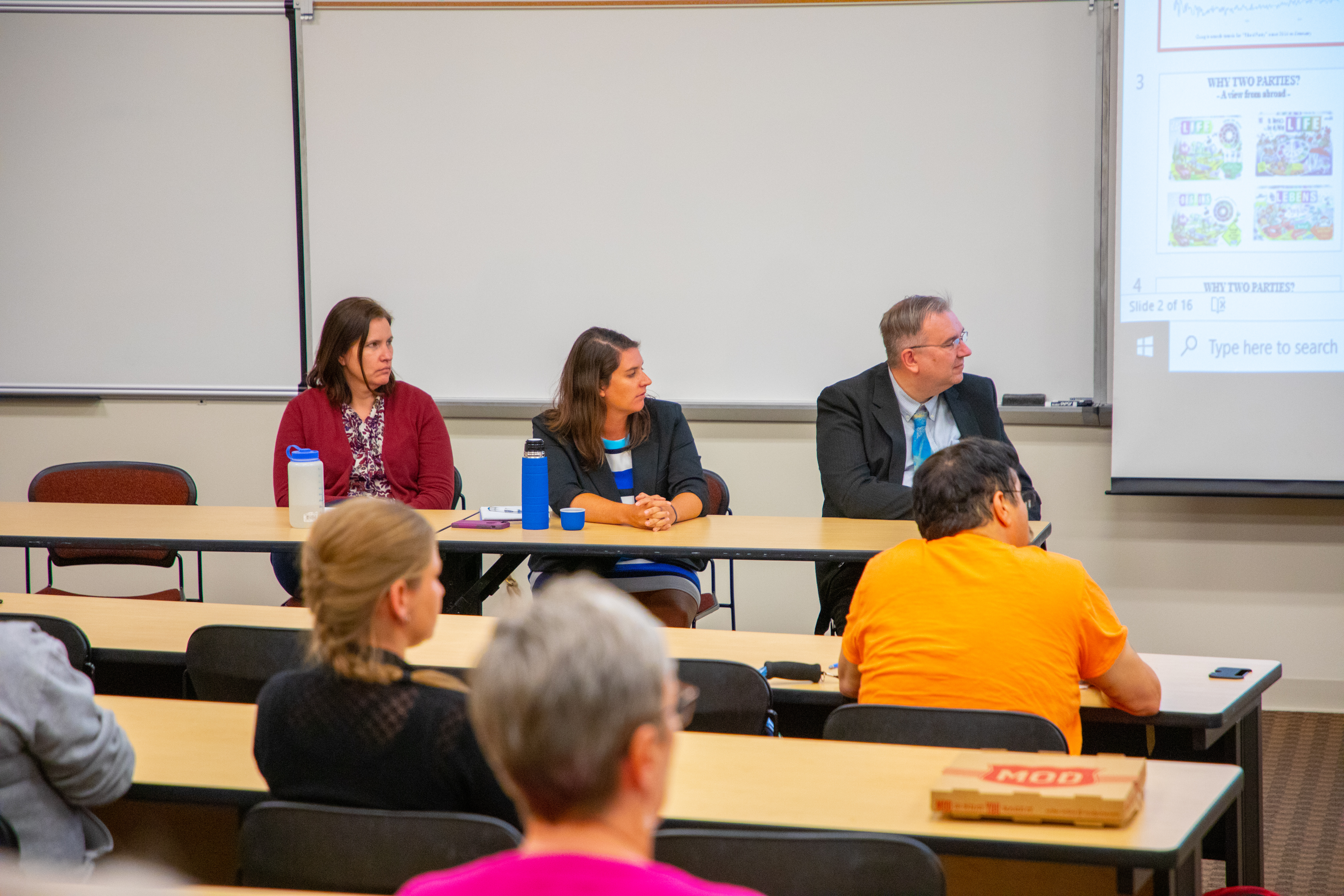 Audience members and three person panel directing attention to screen with information