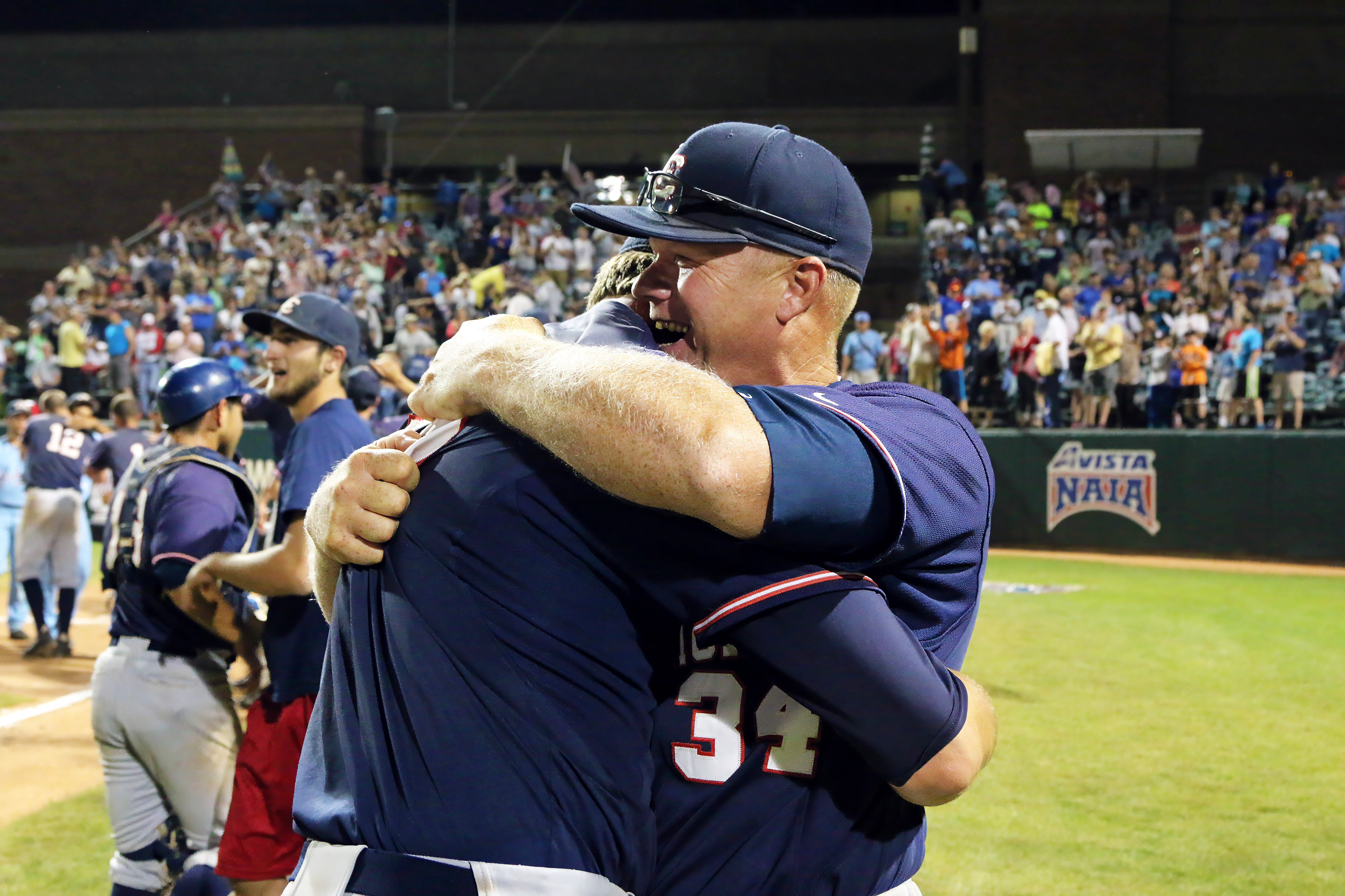 Jeremiah Robbins hugging another person while standing on baseball field and crowd cheers in background