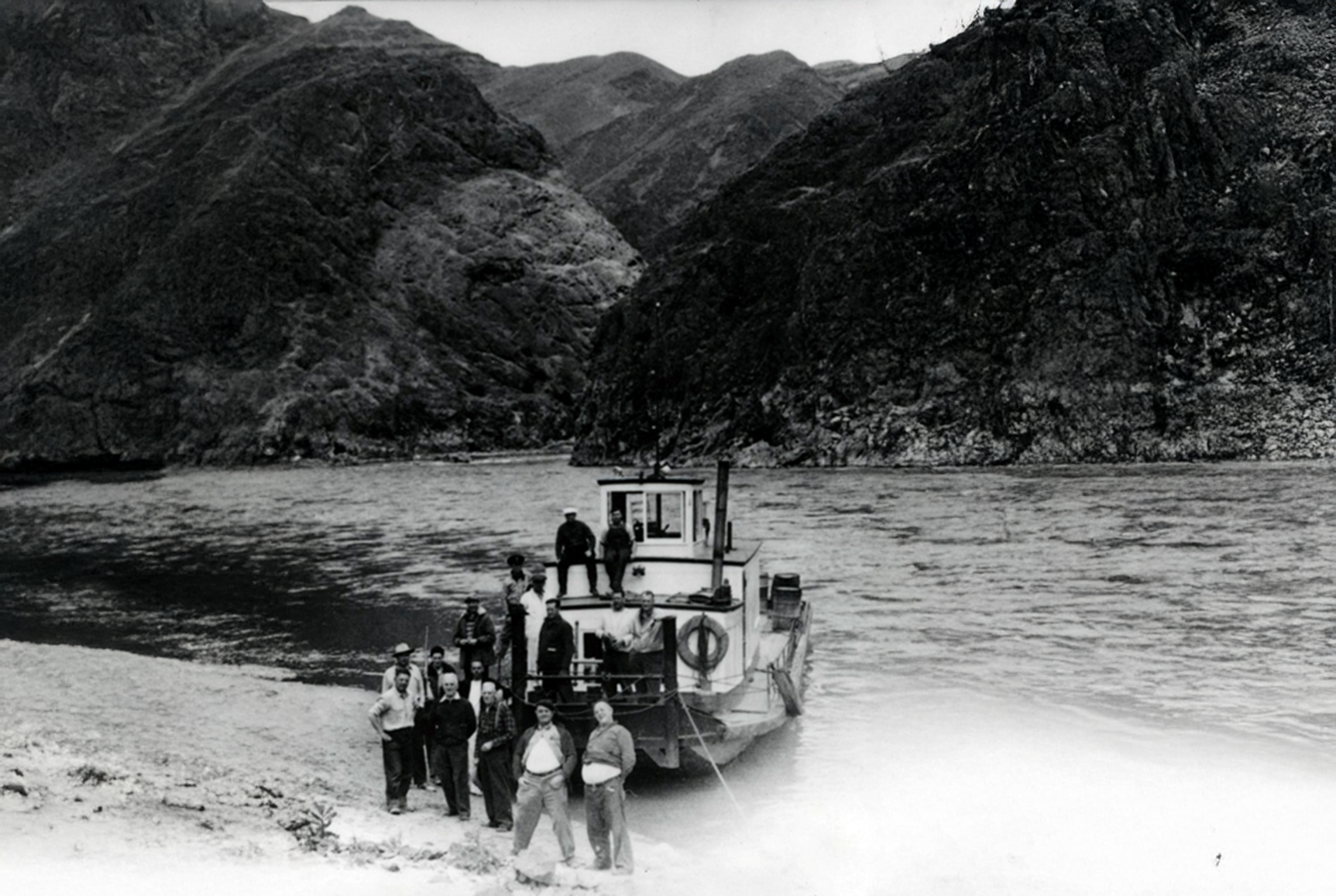 Black and white image with group of men standing on and in front of boat at Hells Canyon