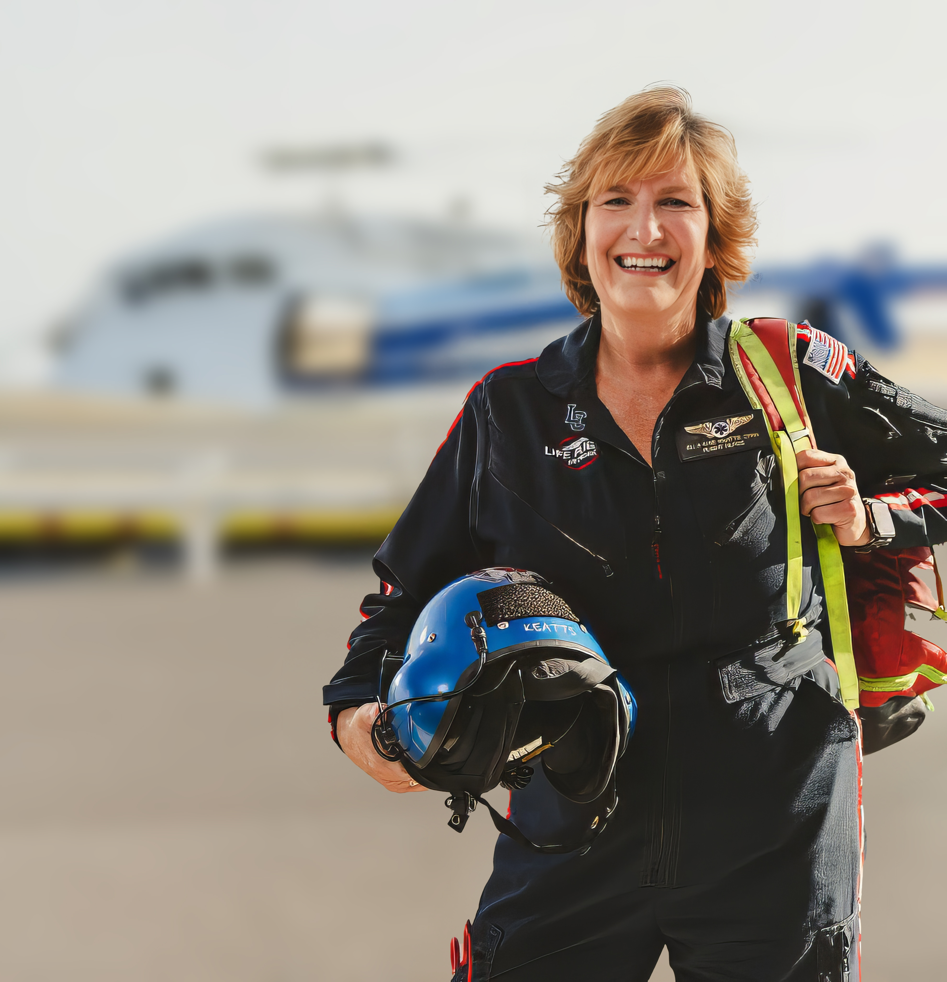 Photo of Associate Professor Ella-Mae Keatts wearing Life Fight uniform, carrying helmet, in front of helicopter 
