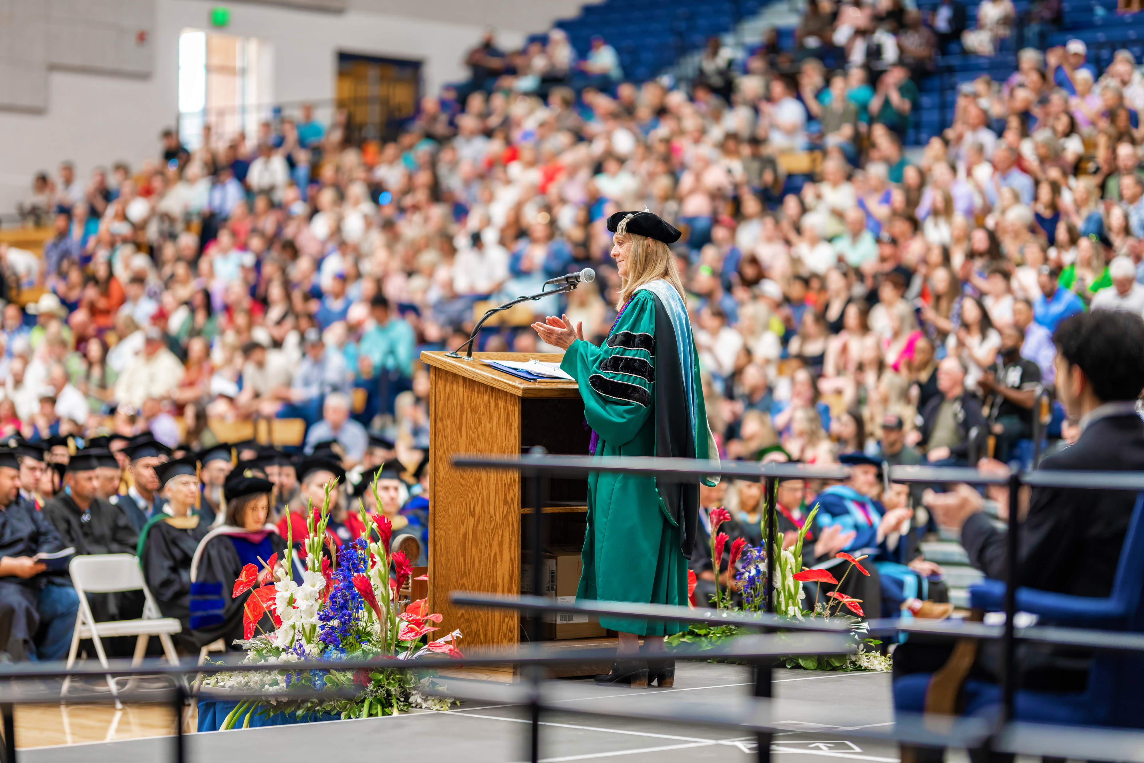 President Pemberton dressed in graduation regalia clapping behind podium looking out at graduation group