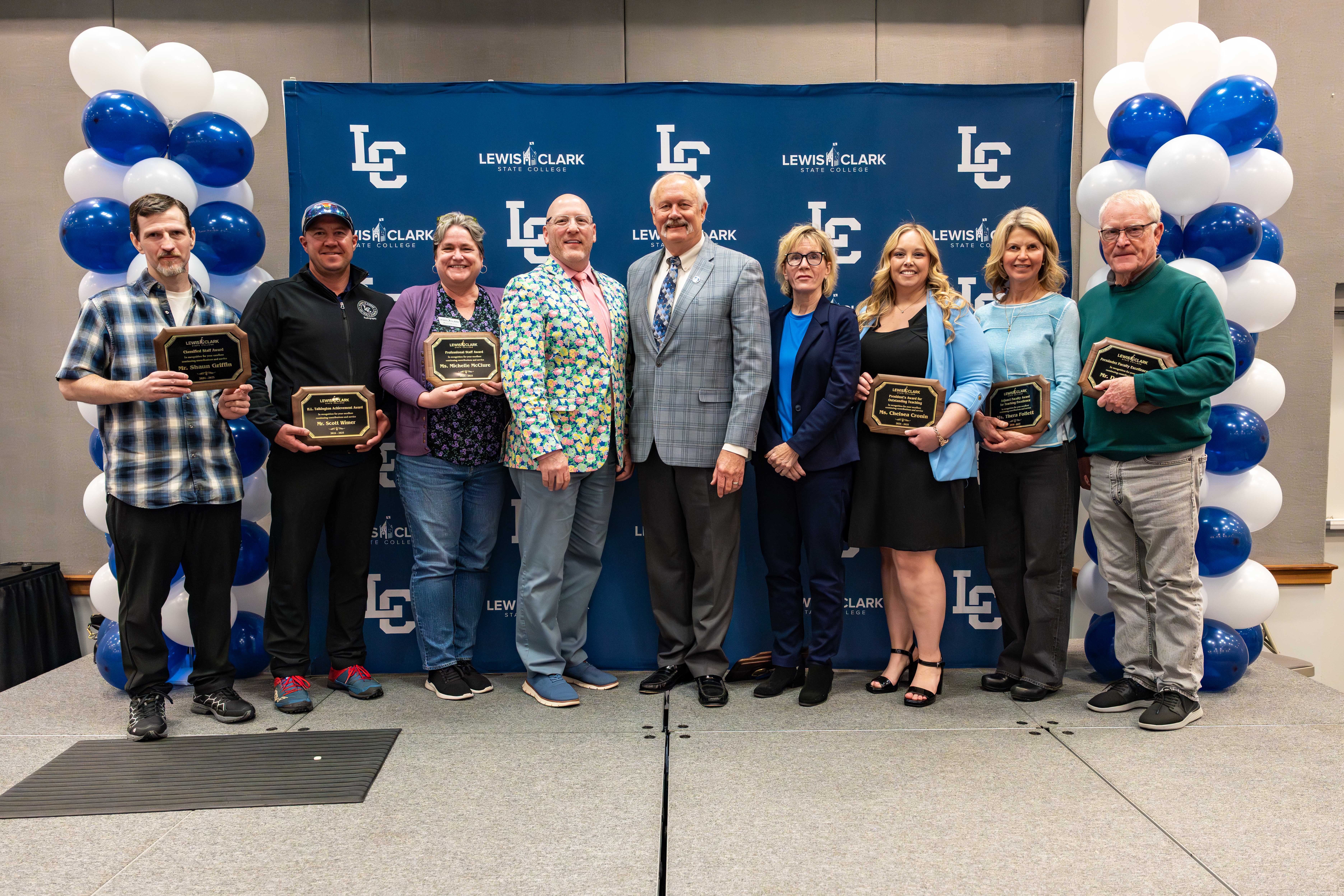 Group of faculty and staff members pose with awards on stage in front of balloons and LC State backdrop
